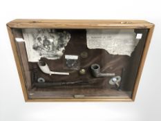 A reproduction glazed montage containing antique pipe, coins, etc.