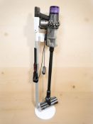 A Dyson cordless stick vacuum cleaner and charging stand.
