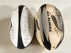 Two New Zealand All Blacks rugby balls bearing many signatures.