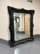 An antique style ornate black painted bevelled mirror,