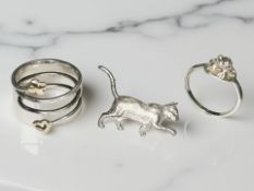 A silver cat brooch, a ring surmounted by a frog, and another silver and yellow metal ring.