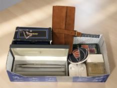 A small group of perfumes, Parker pen, Apple earbuds, a suede money roll.