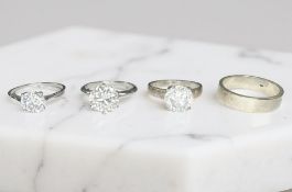 Three silver solitaire dress rings and a band ring.
