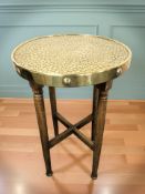 An embossed brass circular occasional table on oak support, height 77 cm.