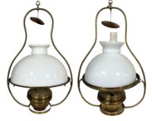 A pair of brass hanging oil lamps with opaque shades and clear glass chimneys, each 65 cm high.
