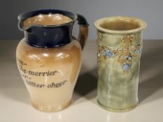 A Royal Doulton stoneware motto jug and a further Doulton cylindrical vase, height 15 cm.