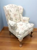 A reproduction carved pine wingback armchair in floral upholstery,