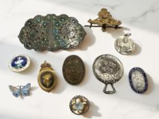 A group of badges, enamel belt buckle, silver brooch, silver backed mirror,