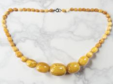A butterscotch amber-coloured bead necklace, the ovoid beads ranging from 3cm to 8mm in width,