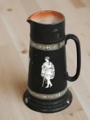 A black glazed ceramic tapering jug decorated with classical figures,