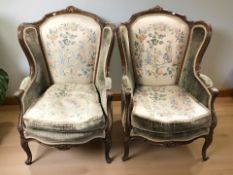 A pair of French carved beech wingback armchairs in green floral upholstery, width 76 cm.