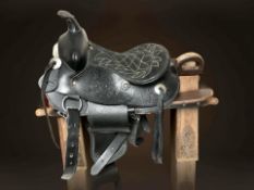 A black leather saddle on a carved wooden saddle stand, length 74 cm.