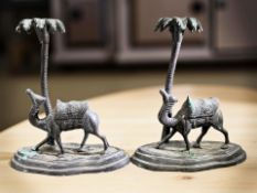 A pair of patinated metal candlesticks in the form of camels beneath palm trees,