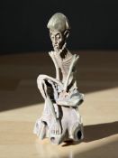 An African silvered metal statue of a seated skeletal figure,