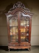 A reproduction heavily carved hardwood glazed double door cabinet with shelved interior,