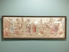 A large gilt framed embroidered panel depicting figures in a middle eastern town square,