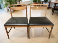 A pair of 20th century teak dining chairs with black vinyl seats.