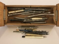 An oak pen box containing assorted writing utensils including several silver propelling pencils,