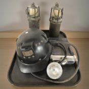 A vintage miner's helmet, torch with battery pack and two lamps.