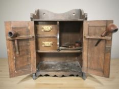 A Victorian carved oak double door smoker's cabinet containing several pipes.