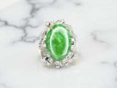 A jade and diamond ring, the polished oval green jade within a raised setting,