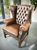 A Chesterfield style deep buttoned brown leather wing back armchair,
