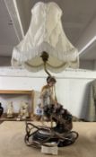 A figural table lamp with a lady pushing a wheel barrow of flowers.