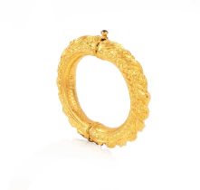 An Indian gold bangle of hinged design with repoussé and engraved floral scroll decoration, the