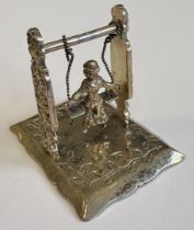 A heavy chased silver table toy in the form of a swing.