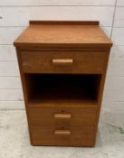 A teak three drawer bedside table with central shelf and on castors (H78cm W47cm D43cm)