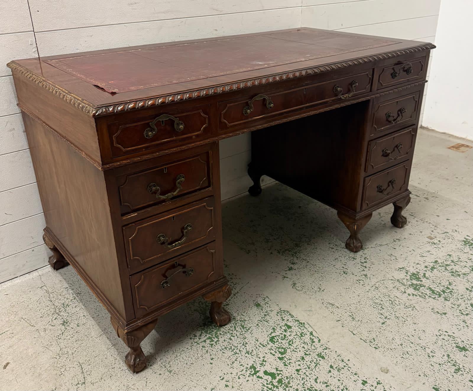 A red leather topped pedestal desk, one long central drawer flanked by eight short drawers and on