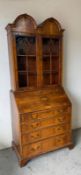 A yew veneered bookcase bureau comprising of an astragal glazed two door bookcase over a four