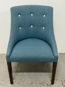 An occasional chair upholstered in blue fabric with white piping, raised on wooden legs.