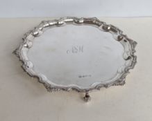 A QEII silver circular salver with ornate pie crust border on three scroll feet, initialled