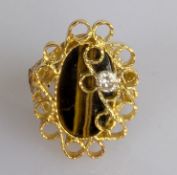 A vintage elliptical tiger eye ring on a yellow gold scroll setting adorned with a diamond
