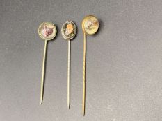 THREE VARIOUS REVERSE PAINTED, BASE METAL STICK PINS