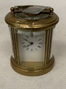A SMALL OVAL BRASS CARRIAGE CLOCK WITH GLASS ESCAPEMENT AND KEY