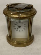 A SMALL OVAL BRASS CARRIAGE CLOCK WITH GLASS ESCAPEMENT AND KEY