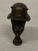 A BRONZE SKULL HEAD PIPE TAMPER