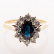 A sapphire and diamond cluster ring, claw set to the centre with an oval-cut dark blue sapphire,