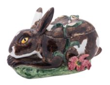 A Continental faience tureen and cover in the form of a crouching rabbit set on a rustic oval base,