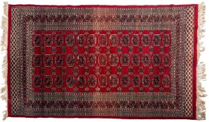 A Pakistan rug, of Turkoman design, the wine red field with three rows of quartered guls,