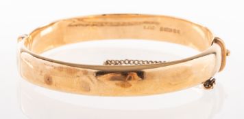 A 1970's 9ct gold bangle, with foliate carving to the front panel, hinged, push in clasp,