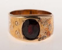 A vintage garnet set ring, the wide band is flush grain set with an oval-cut garnet,