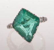 An emerald and diamond ring, claw set in a swaged edge gallery with a kite-shaped emerald,