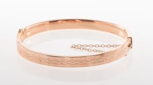 An early 20th century 9ct rose gold hinged bangle, with carved pattern to front section,