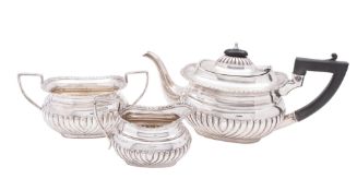 An Edwardian three-piece silver tea set, of rounded oblong form, with part-fluted bodies,