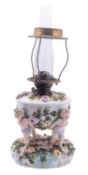 A Continental porcelain oil lamp modelled as four children supporting a florally encrusted reservoir