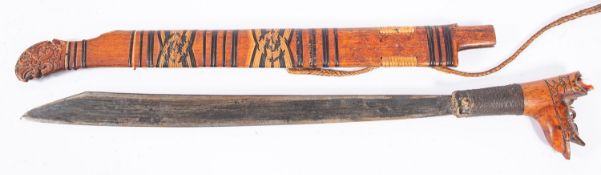 A Dyak Mandu sword, the shaped single edge blade with carved grip in a bound carved wooden scabbard,