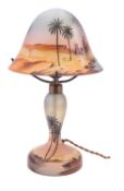A painted glass table lamp and domed shade painted with a figure and camels at a desert oasis,